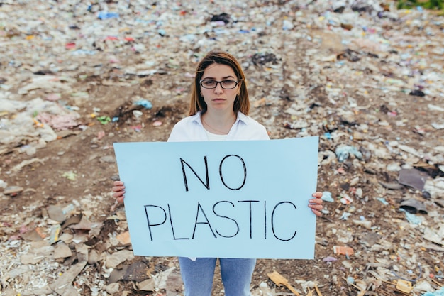 Weibliche Freiwillige demonstriert eine Mülldeponie mit einem Plakat ohne Plastik, Aktivistin kämpft mit Umweltverschmutzung