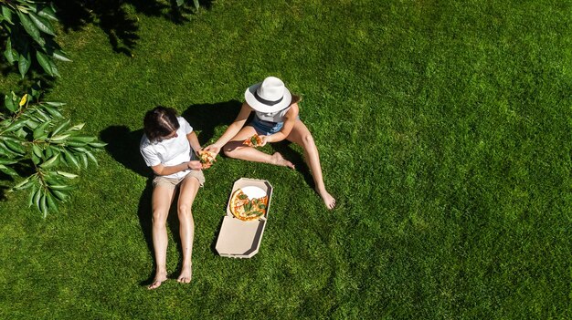 Foto weibliche freunde essen pizza bei einem sommerpicknick im park, entspannen sich auf dem gras und haben spaß mit der aussicht aus der luft