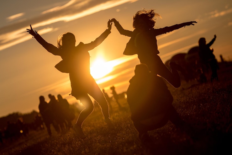 Foto weibliche freunde springen, während der mann während des sonnenuntergangs im park hockt