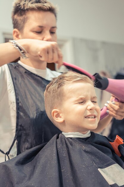 Weibliche Friseurin stylt die Haare eines Jungen im Salon