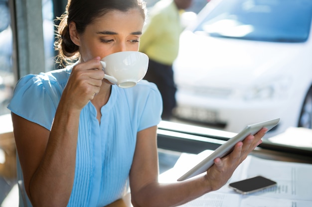 Weibliche Führungskraft, die digitales Tablett beim Kaffeetrinken verwendet