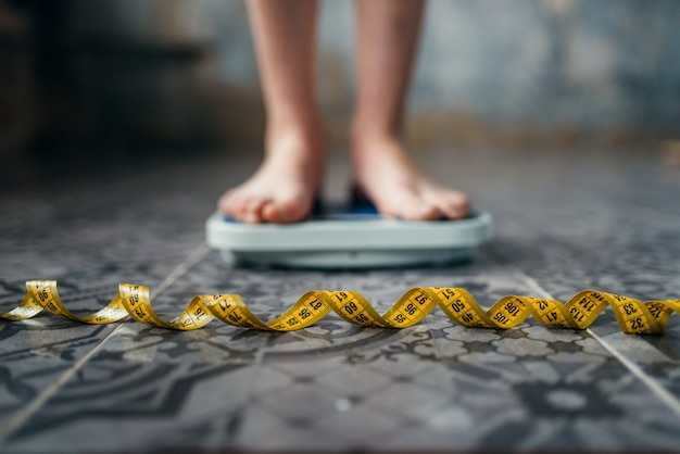 Weibliche Füße auf der Waage, Maßband. Konzept zur Fett- oder Kalorienverbrennung. Gewichtsverlust, harte Diät