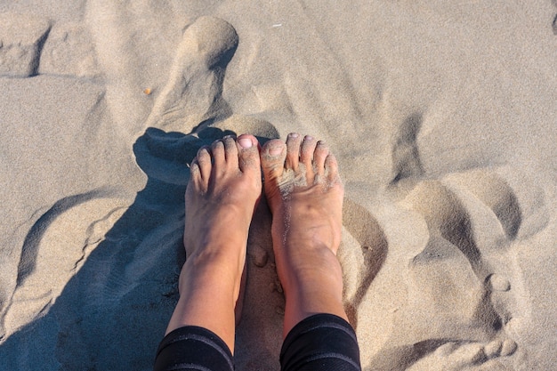 Weibliche Füße im Sand am Strand mit schwarzen Hosen