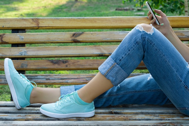 Weibliche Füße in der Blue Jeans und in einer Nahaufnahme des Handys in der Hand