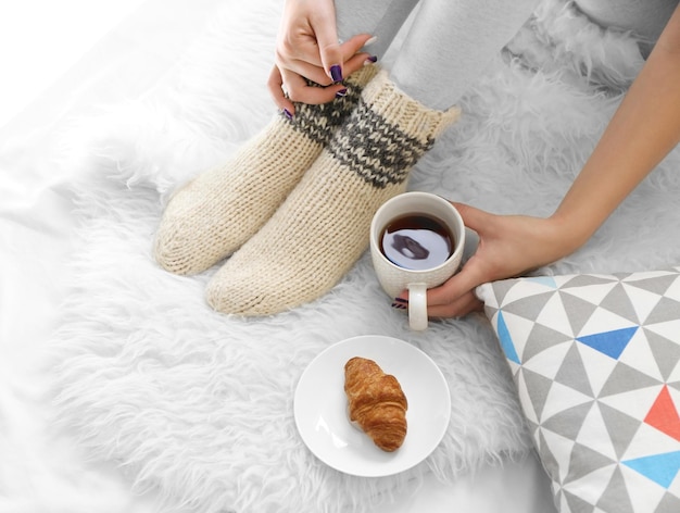 Weibliche Füße in Socken mit Tasse Tee auf flauschiger Decke