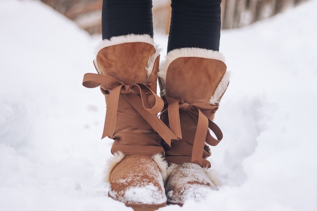 Weibliche Füße in warmen Stiefeln im Winter auf Schneeboden Closeup