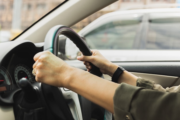 Weibliche Hände am Lenkrad eines Autos während der Fahrt auf der Straße.