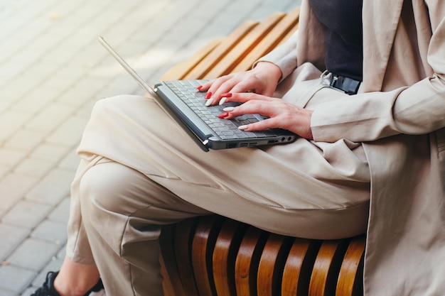 Weibliche Hände auf der Laptop-Tastatur Eine Frau sitzt auf einer Bank auf der Straße Nicht erkennbares Bild