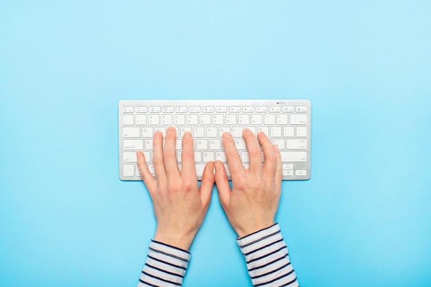 Weibliche Hände auf einer Tastatur auf einer blauen Oberfläche. Konzept der Büroarbeit, freiberuflich, online. . Flachgelegt, Draufsicht