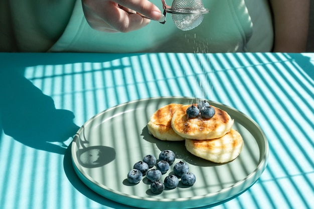 weibliche hände bestreuen pfannkuchen mit puderzucker