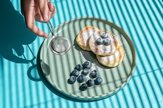 weibliche hände bestreuen pfannkuchen mit puderzucker