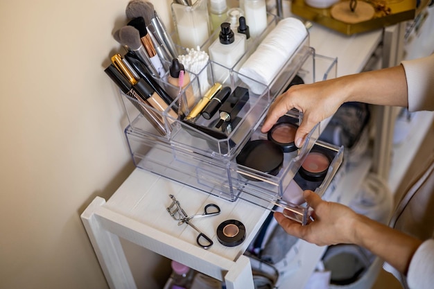 Foto weibliche hände der nahaufnahme, die luxuskosmetik in acrylkasten mit schubladenspeicherorganisation setzen