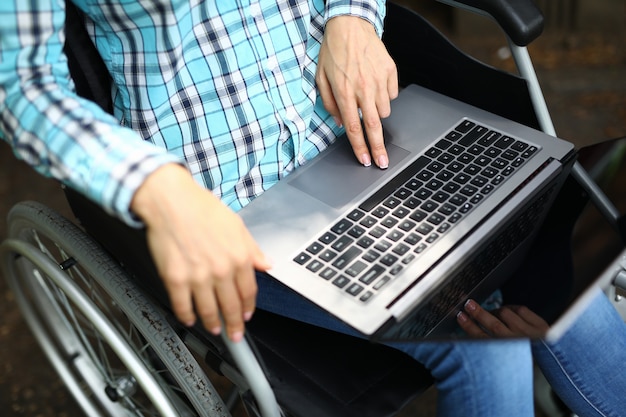 Weibliche Hände, die am Laptop arbeiten, während sie im Rollstuhl sitzen