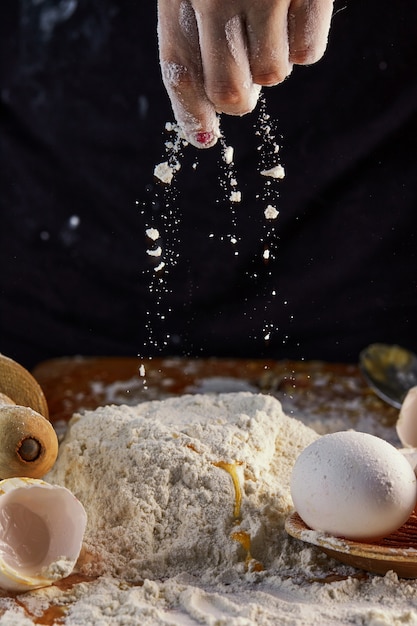 Weibliche Hände, die dem Teig Mehl hinzufügen und den Teig zum Backen kneten