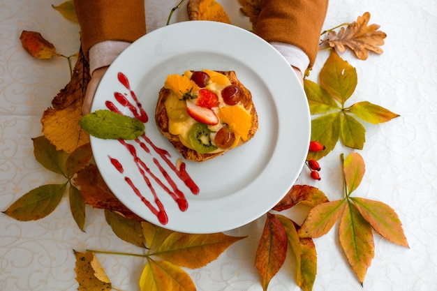 Weibliche Hände, die den weißen Teller mit Obstkuchen halten