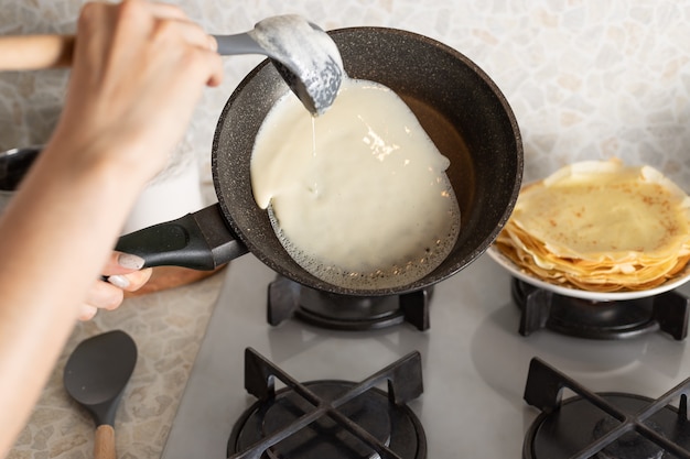 Weibliche Hände, die dünne Pfannkuchen auf Bratpfanne kochen