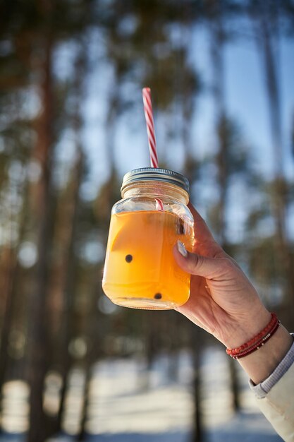 Weibliche Hände, die ein Glas Glühwein auf einem Winterwald halten