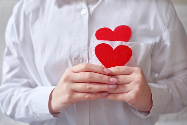 Weibliche Hände, die ein Herz und eine Form des Herzens in der Tasche des weißen Hemdmedizininhalts halten