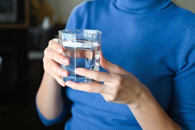 Weibliche Hände, die ein klares Glas Wasser halten. Ein Glas sauberes Mineralwasser in den Händen, gesundes Getränk während der Krankheit.