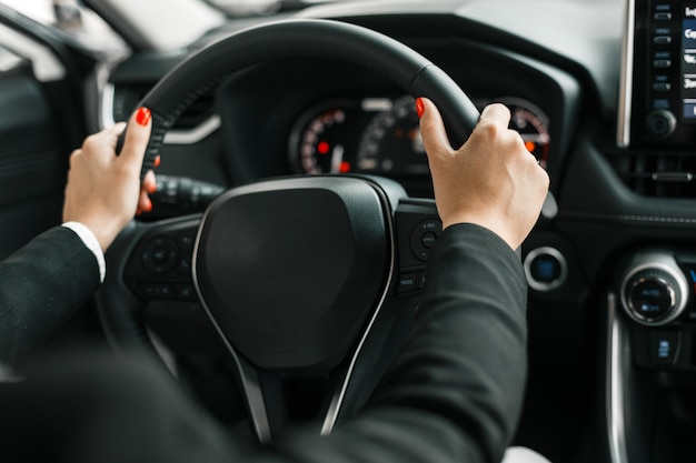 Weibliche Hände, die ein Lenkrad im Autosalon halten.