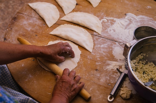 Weibliche Hände, die ein Nudelholz beim Kochen von Kutaba oder Chebureks halten Hackfleisch und Zwiebeln im TeigHüttenkäse und Zwiebeln im Teig Aserbaidschanische tatarische kaukasische griechische Küche