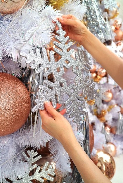 Weibliche Hände, die eine Funkelnschneeflockenverzierung auf Weihnachtsbaum hängen