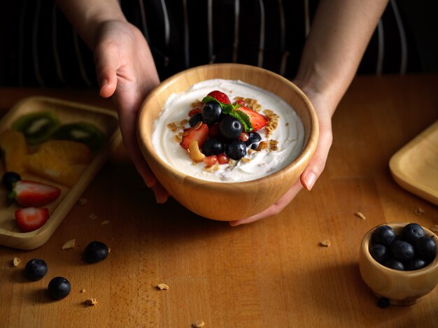 weibliche Hände, die eine Schüssel Müsli mit natürlichem griechischem Joghurt und frischen Beeren halten