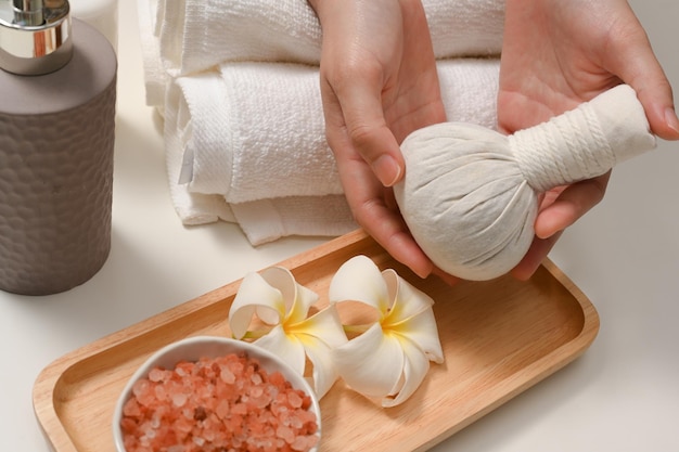 Weibliche Hände, die einen Massagestempel oder einen Spa-Kräuterball oder einen Massageball in Spa-Tisch-Kompositionen halten