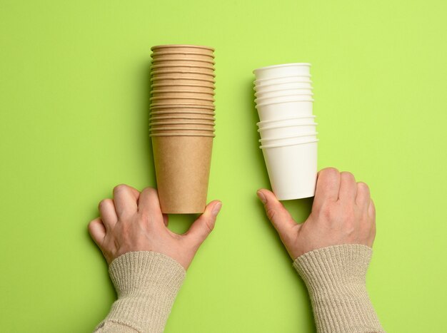 Foto weibliche hände, die einen stapel einwegbecher aus braunem und weißem papier halten, schließen oben