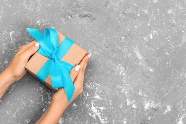 Weibliche Hände, die Geschenkbox mit blauem Band auf grauem Hintergrund halten