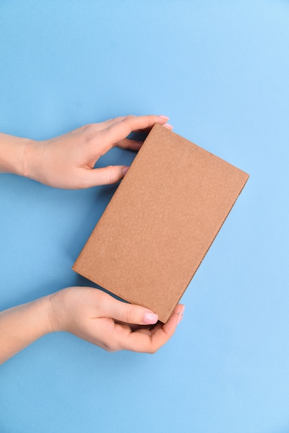 Weibliche Hände, die Geschenkbox oder Geschenkbox-Paket im Bastelpapier über blauem Hintergrund halten. Draufsicht, flach liegen