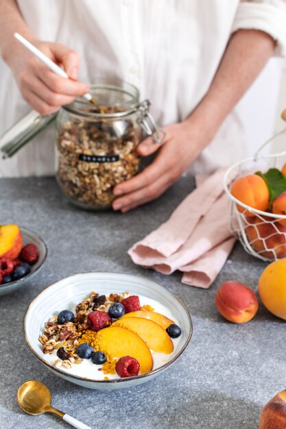 Weibliche Hände, die Granola vom Glas, Granola mit frischem Pfirsich des griechischen Joghurts dienen