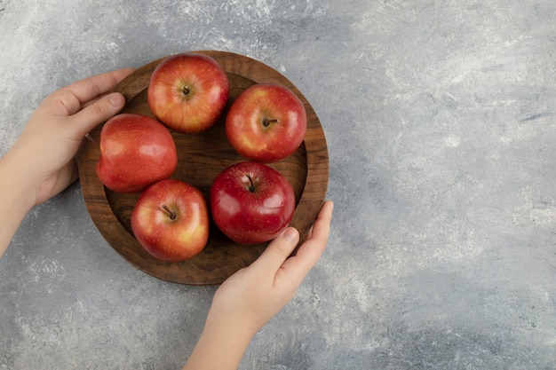Weibliche Hände, die Holzplatte der roten Äpfel auf Marmoroberfläche halten.