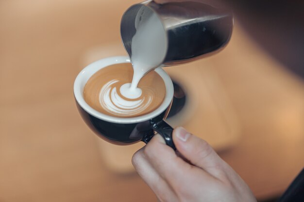 Weibliche Hände, die Kaffee mit Milch verzieren und Latte Art machen