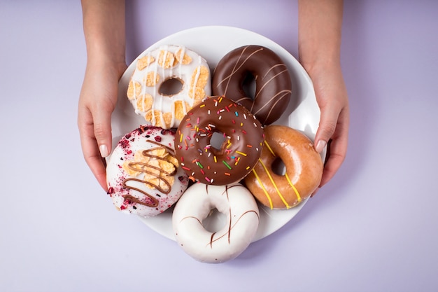 Weibliche Hände, die köstliche Donuts auf einem Teller halten - Draufsicht lila Hintergrund
