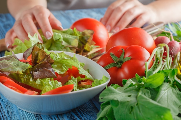 Weibliche Hände, die Kopfsalatblätter in Schüssel mit Salat, Nahaufnahme hinzufügen