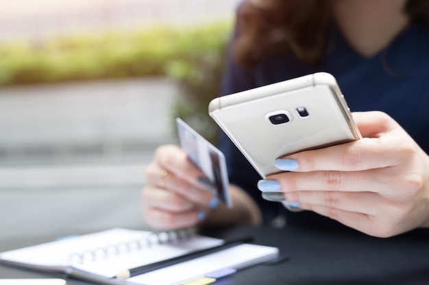 Weibliche Hände, die Kreditkarte halten und Telefon benutzen.