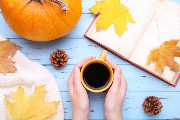 Weibliche Hände, die Schale schwarzen Kaffee mit Herbstlaub halten