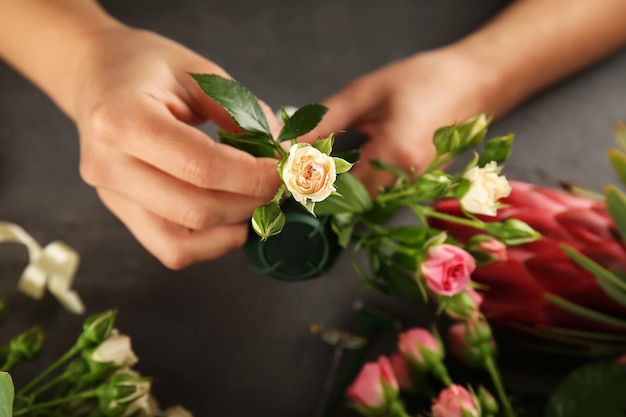 Weibliche Hände, die schönen Blumenstrauß auf dunkler Oberfläche machen