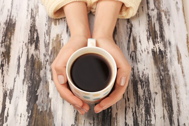 Weibliche Hände, die Tasse Kaffee auf hölzernem Hintergrund halten holding