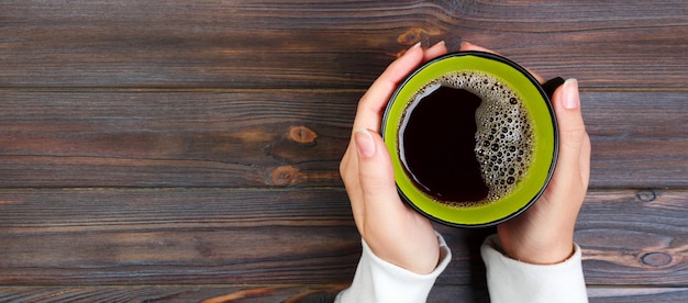 Weibliche Hände, die Tasse Kaffee auf rustikalem Holztisch halten