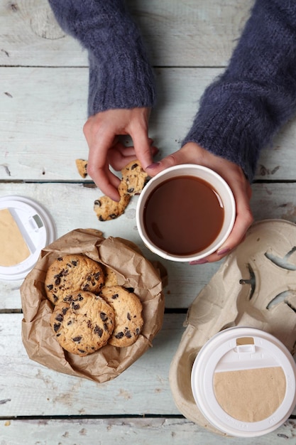 Foto weibliche hände, die tasse kaffee und kekse auf hölzernem tisch nah halten