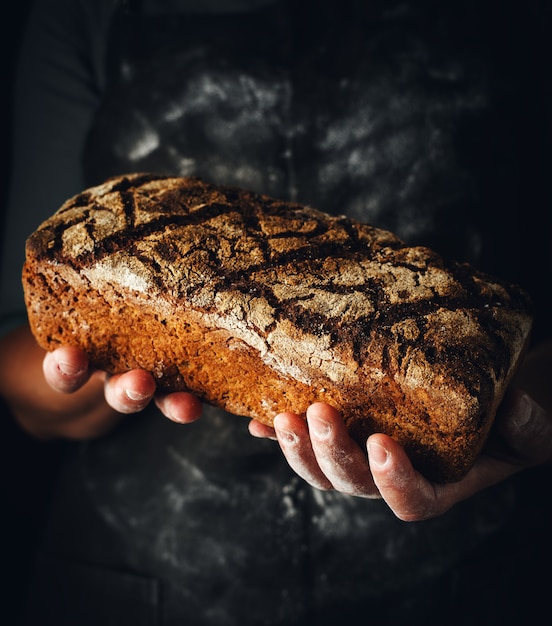 Weibliche Hände halten dunkles Roggenbrot.