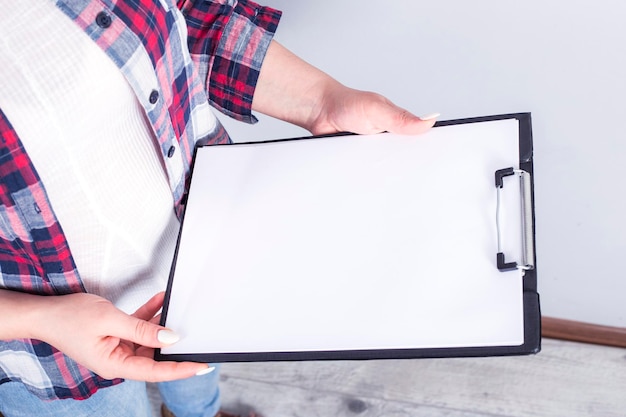 Weibliche Hände halten ein Blatt Papier oder ein Notizbuch und einen Bleistift