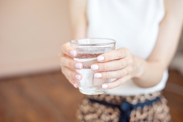 Weibliche Hände halten ein klares Glas Wasser. Ein Glas sauberes Mineralwasser in Händen, gesundes Getränk.