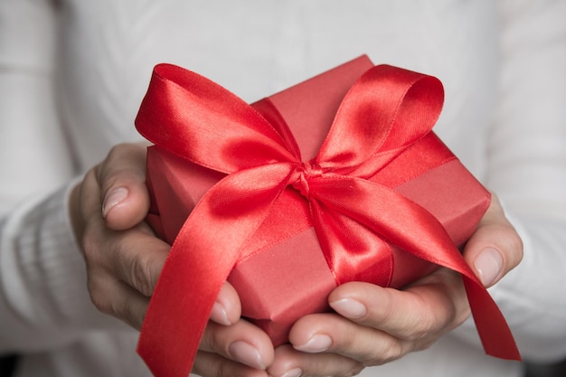 Weibliche Hände halten ein rotes Geschenk, das mit einer roten Schleife zu Weihnachten verpackt ist
