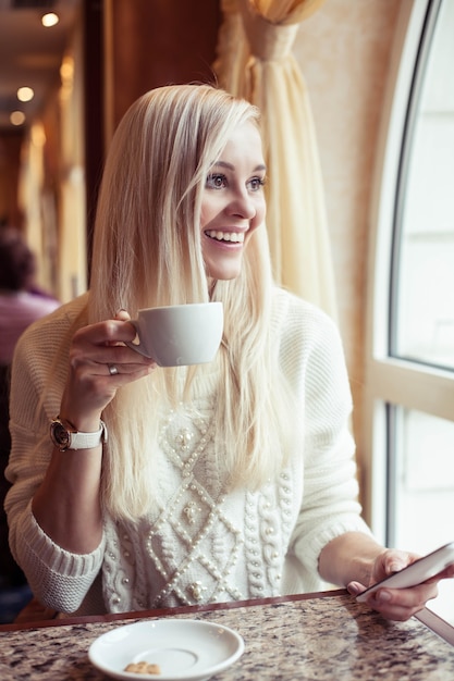 Weibliche Hände halten eine Tasse heißen Kakao. Eine junge Frau sitzt in einem gemütlichen Café. Das Mädchen trinkt Kakao. Winter. Gemütlicher Herbst.