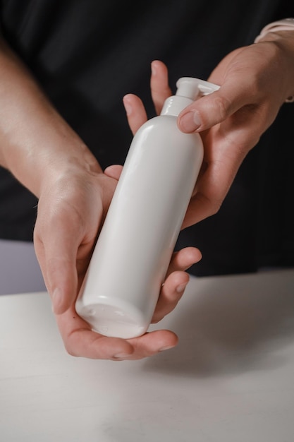 Weibliche Hände halten eine weiße Kosmetikflasche auf weißem Hintergrund für Hautpflege und reine Schönheit.