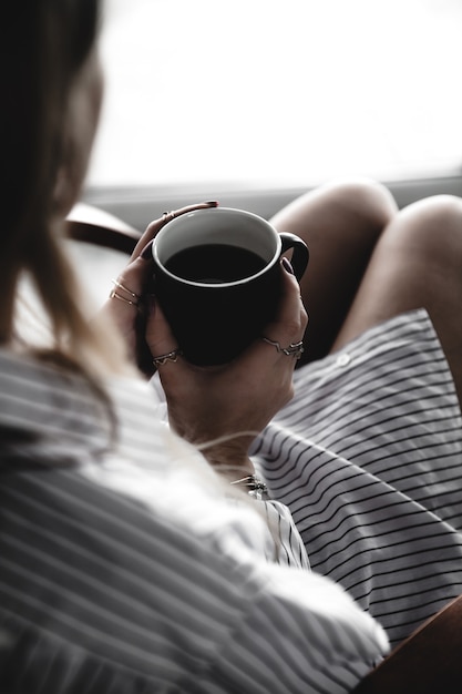 Weibliche Hände halten eine weiße Tasse Tee, burgunder Maniküre, das Mädchen ist in ein Hemd gekleidet