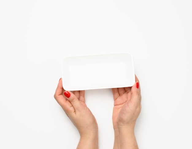 Weibliche Hände halten einen leeren rechteckigen Einweg-Kunststoffbehälter auf weißem Hintergrund, Draufsicht